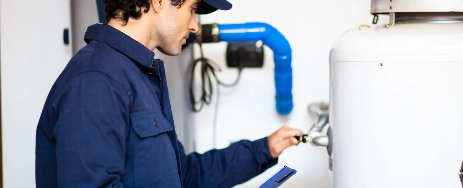 A technician inspecting a water heater, holding a clipboard and adjusting a valve.