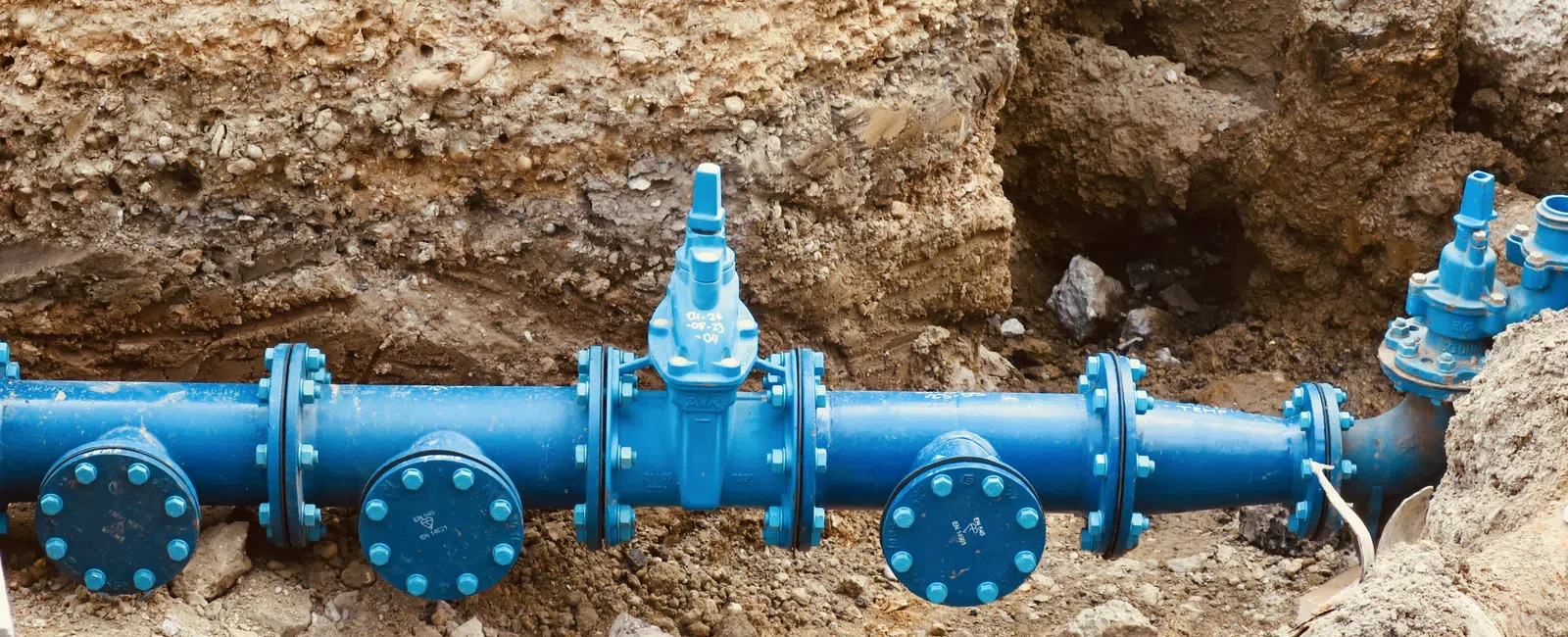 Blue underground water pipeline with multiple valves installed in soil trench for utility service.