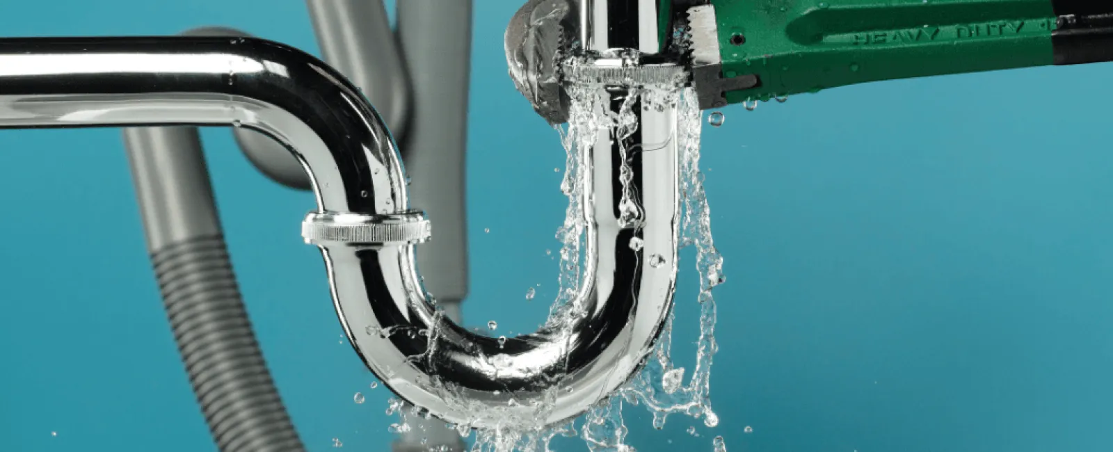 Leaking chrome plumbing pipe being tightened with green pipe wrench against blue background