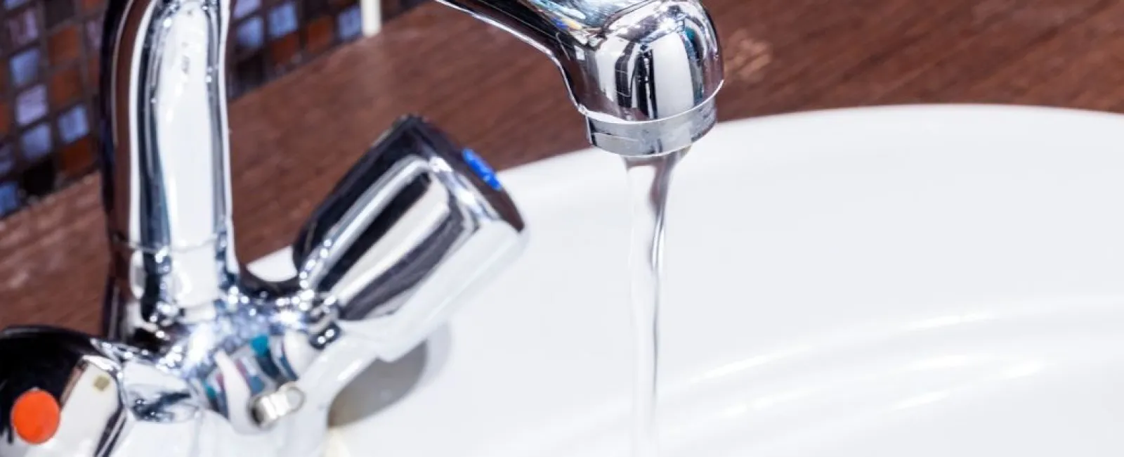 Chrome faucet with water flowing into a white sink against a mosaic tile backsplash