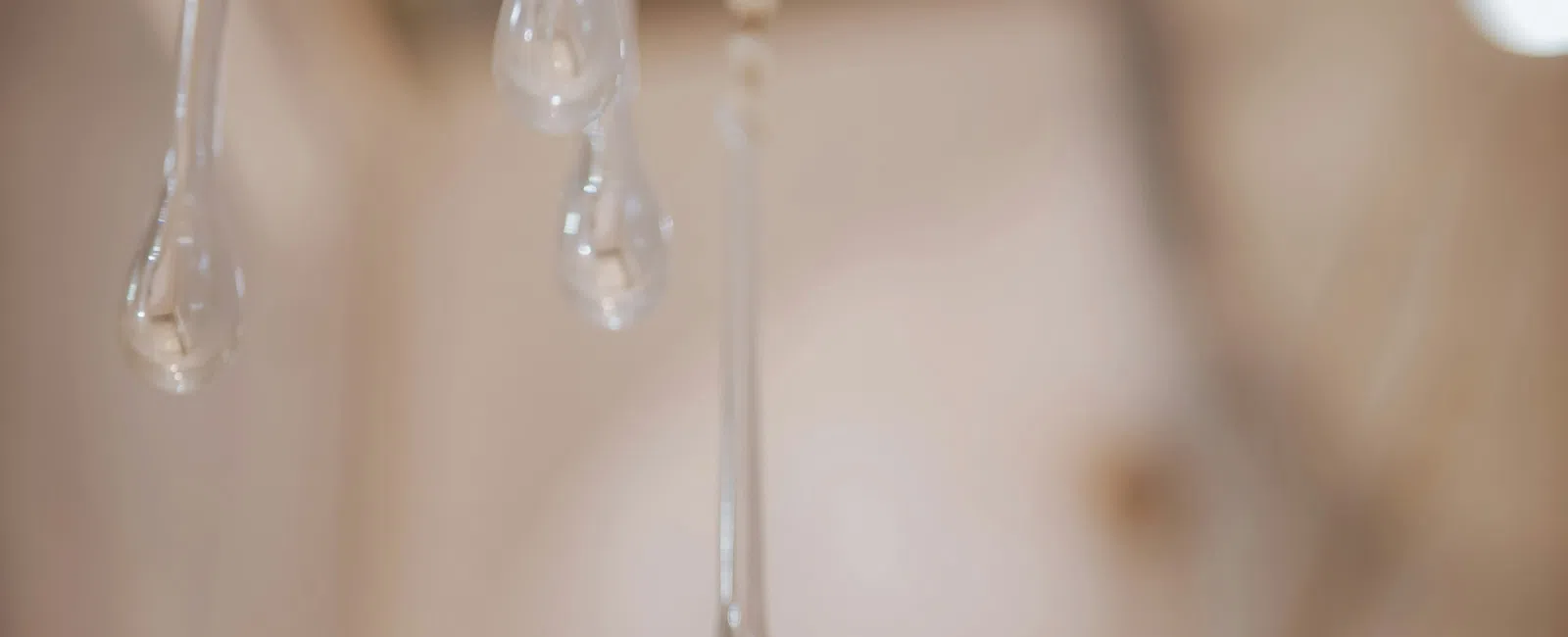 Close-up of delicate glass droplets hanging from thin strands against a soft beige background.