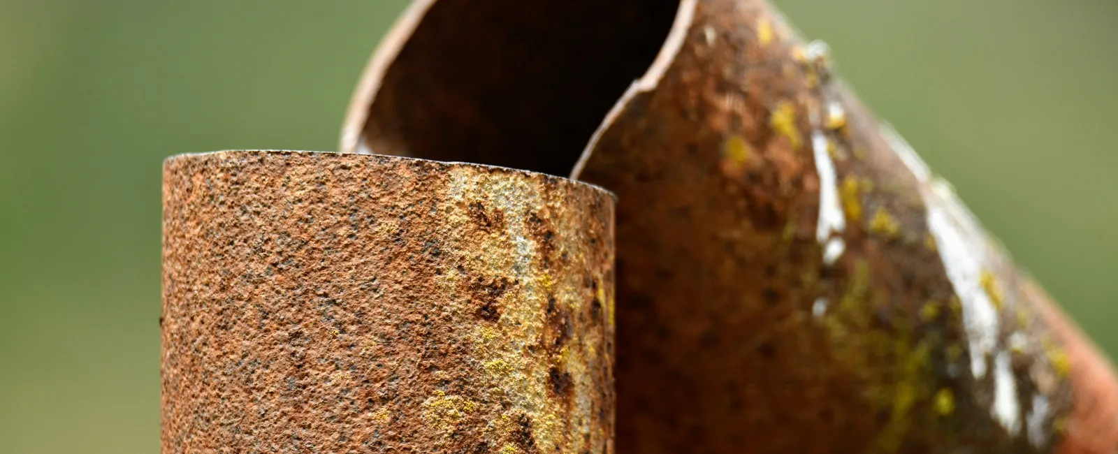 Close-up of two rusted metal pipes with textured corroded surfaces against a blurred green background