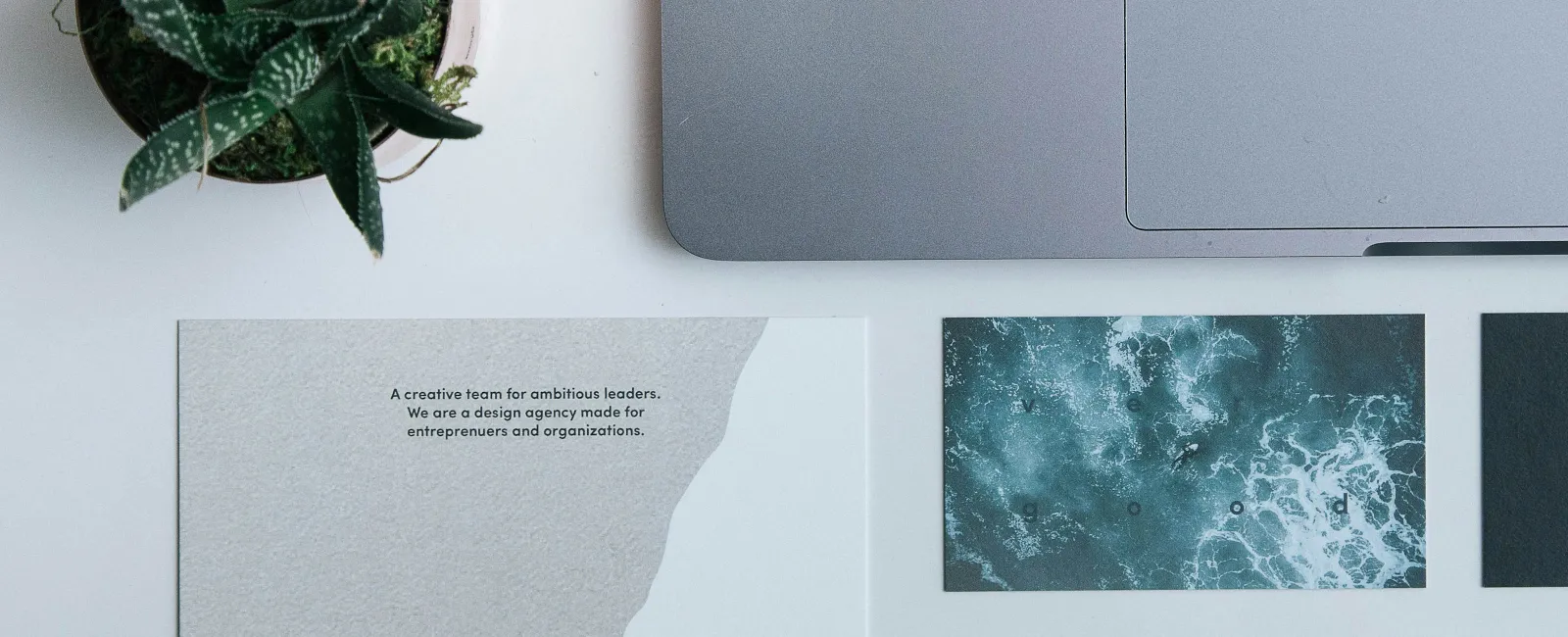 Workspace featuring a laptop, two succulents, and Very Good Creative Co. branded business cards and brochure.