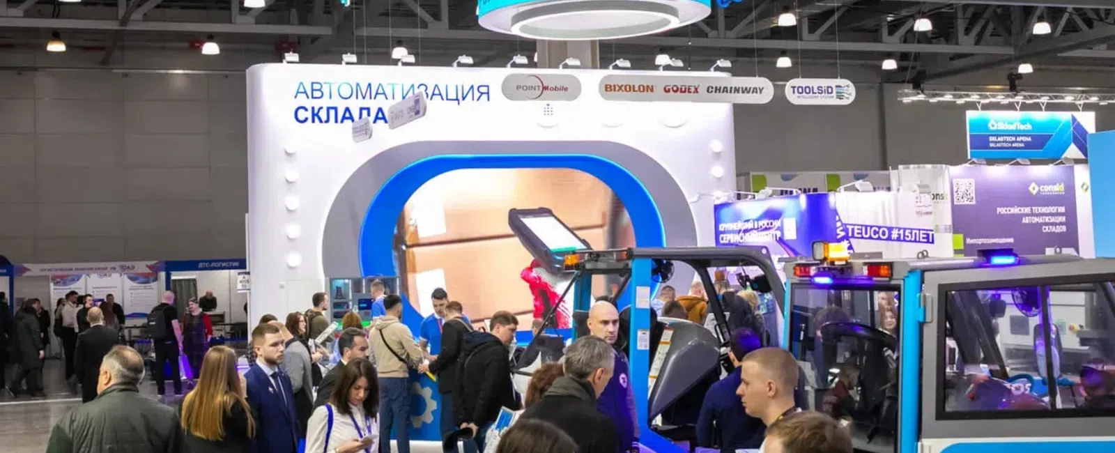 Crowded trade show booth of Ateuco featuring warehouse automation technology and machinery with attendees interacting.
