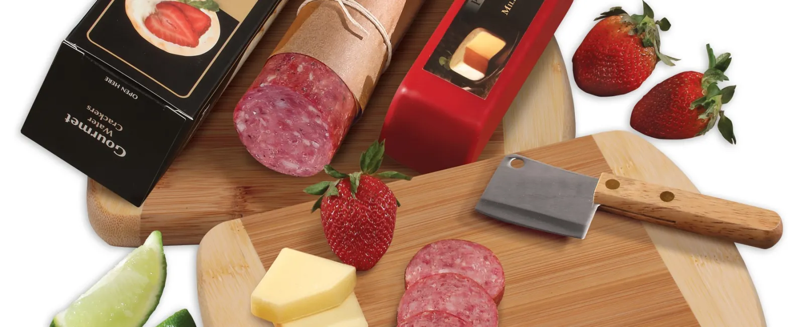 Sliced salami, cheese, cracker box, strawberries, lime wedges, and a cleaver on wooden cutting boards.