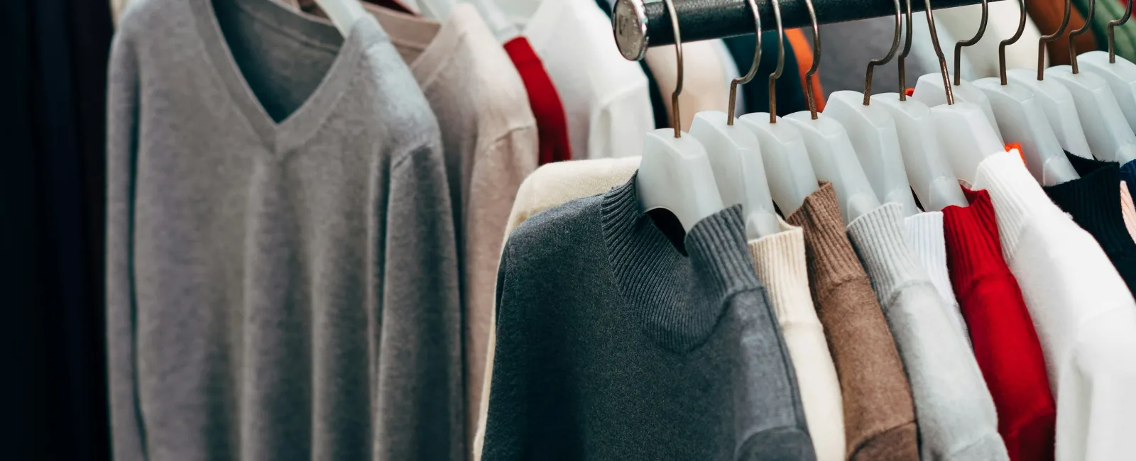 Rows of sweaters in various colors hanging on racks at a clothing store or market display.