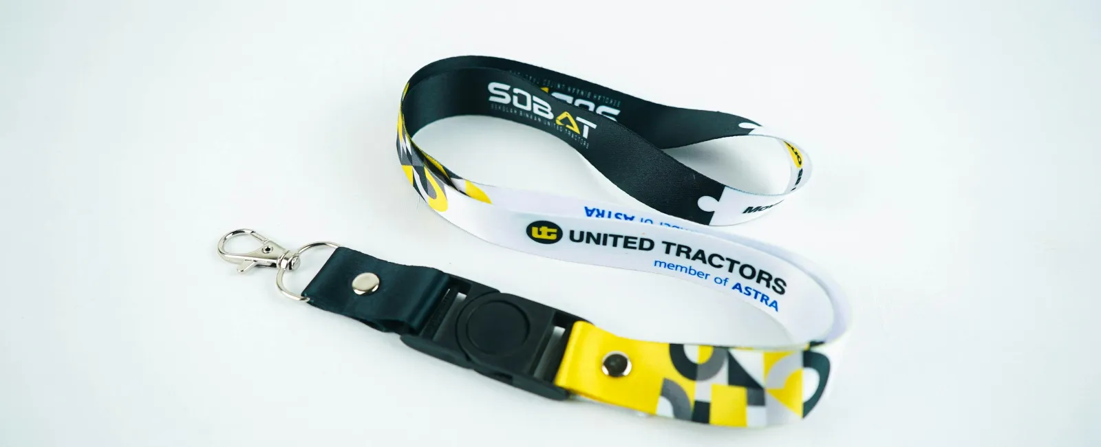 Black and white United Tractors lanyard with yellow accents and metal clip on a white background.