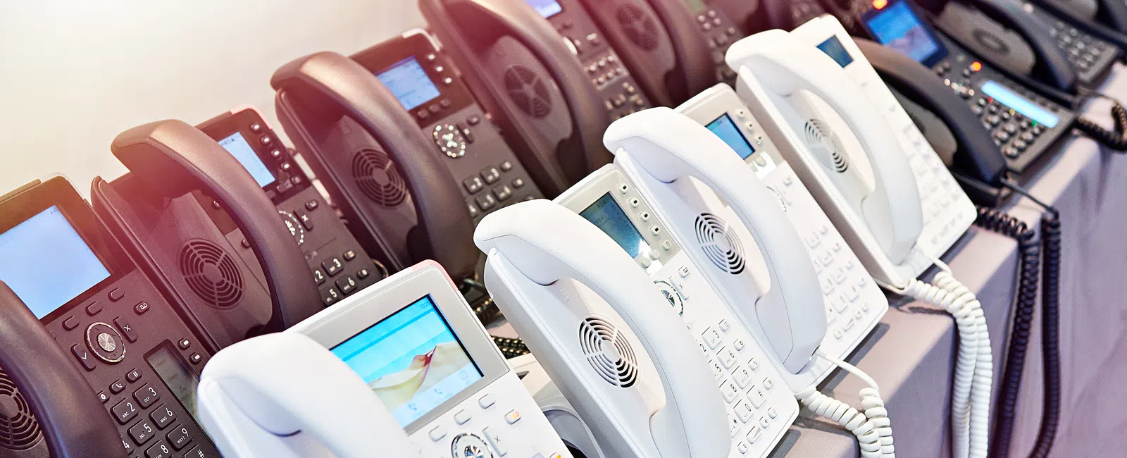 Row of modern white and black office desk phones with digital displays lined up on a table.