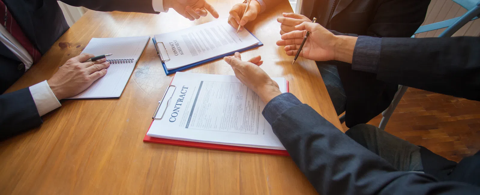 Business professionals discussing and signing contracts around a wooden table in a bright office setting.