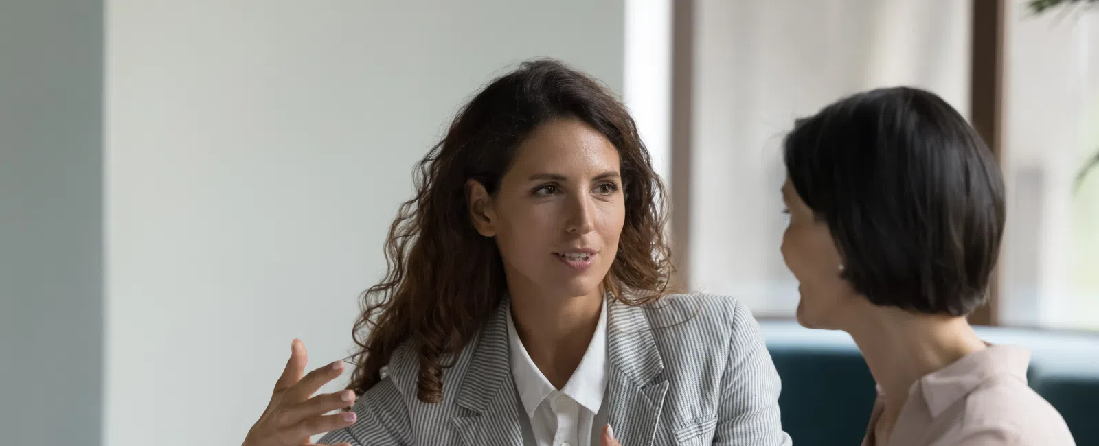 Two professional women engaged in a discussion at a laptop in a modern office setting.