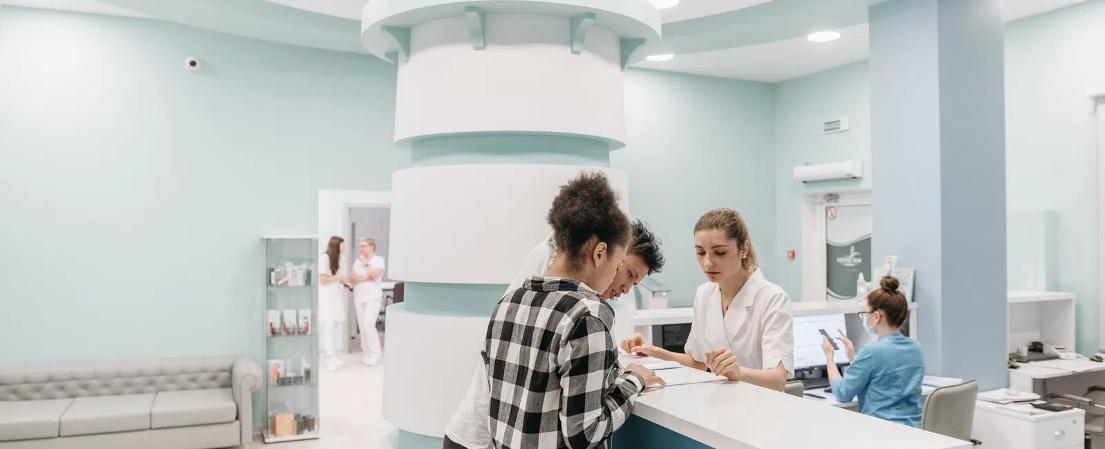 Couple consulting with receptionist at modern medical clinic reception desk with staff in background.