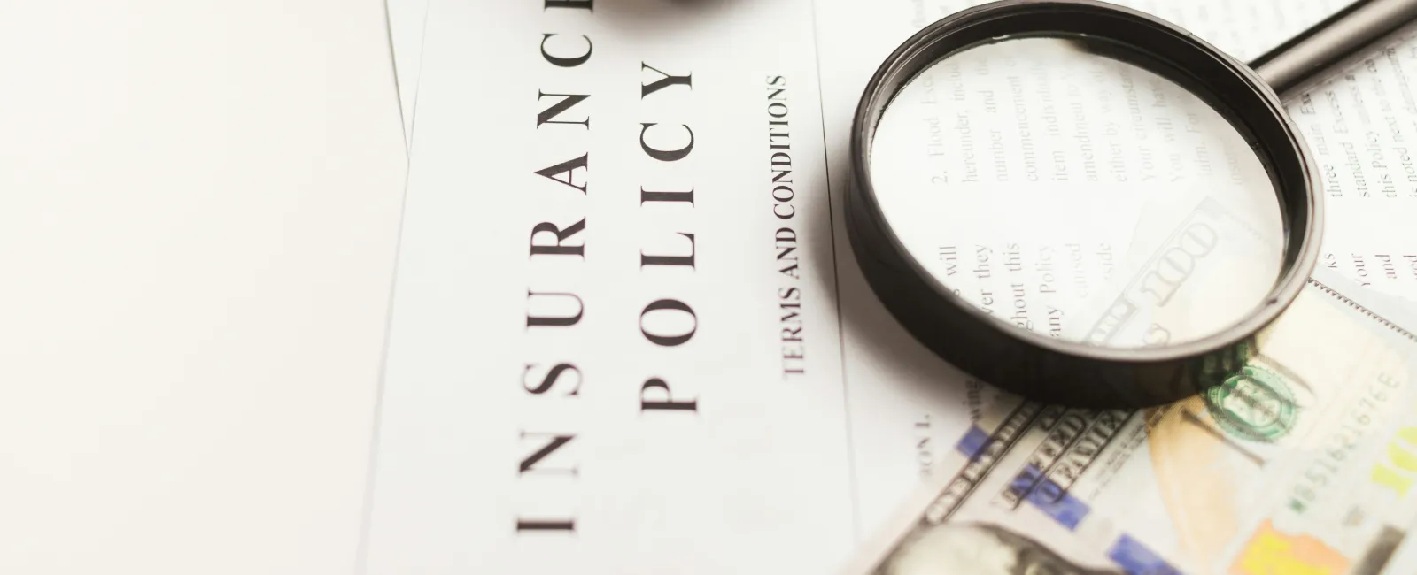 Magnifying glass on insurance policy documents with toy car and US dollar bills, emphasizing coverage and finance.