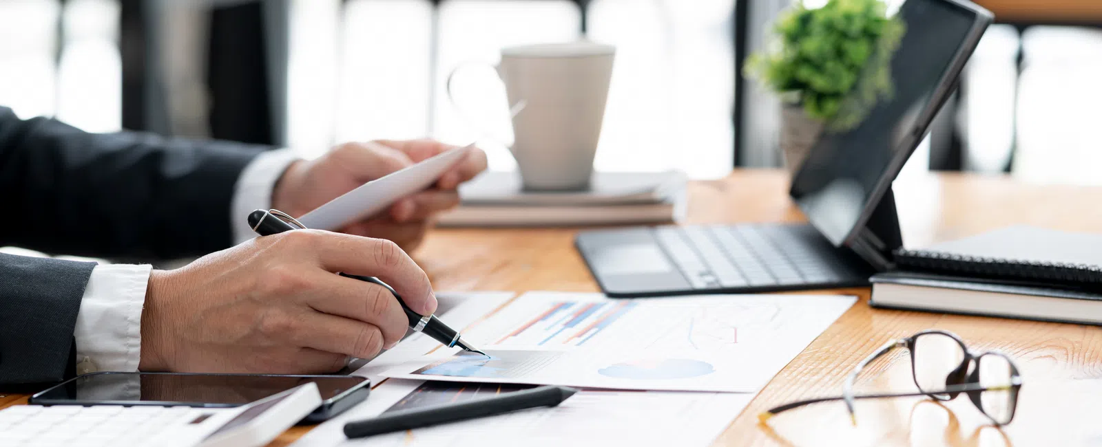 Business professional analyzing financial charts and graphs on paper with tablet, laptop, and glasses on desk