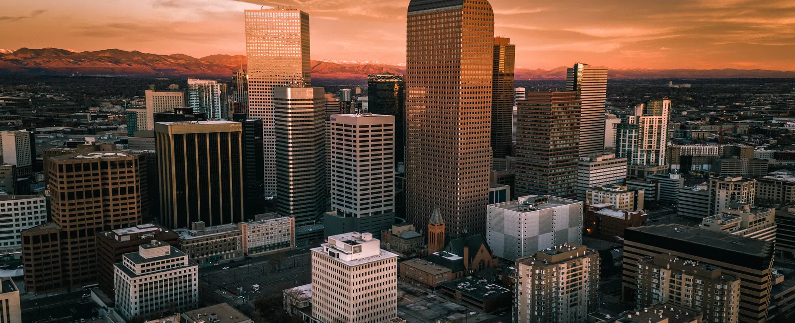 Downtown city skyline with tall skyscrapers during a warm sunset and mountains in the background.