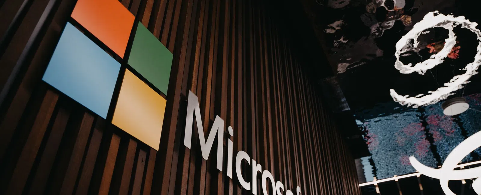 Microsoft logo with colored squares on a dark vertical wood panel wall and abstract reflections on ceiling