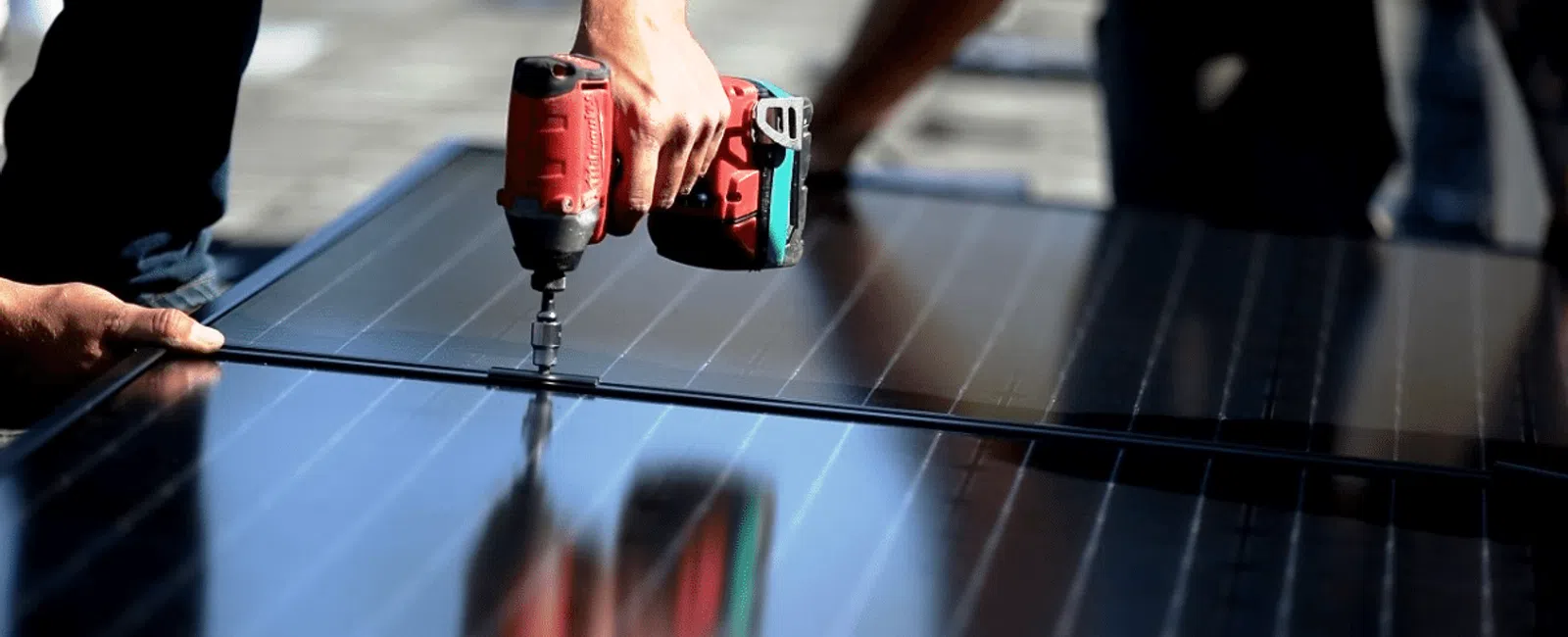 Worker using a drill to install solar panels on a rooftop under sunny conditions