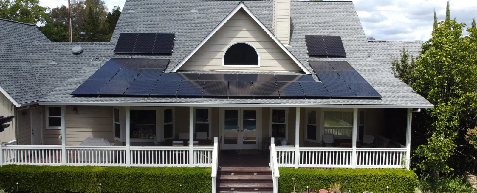 Suburban house with a gray roof featuring solar panels on a sunny day with a green lawn and blue sky.