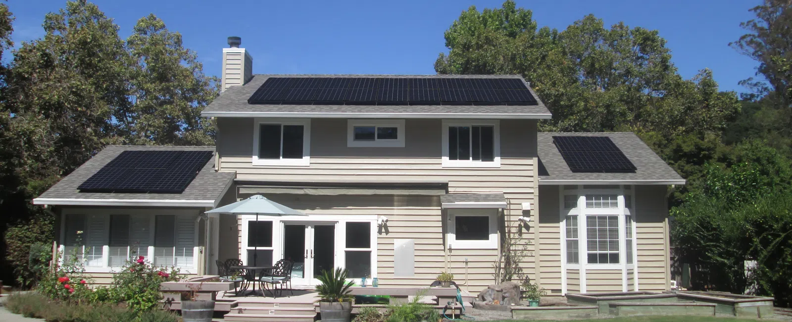 Two-story house with solar panels on the roof and a swimming pool in the backyard under a clear blue sky.