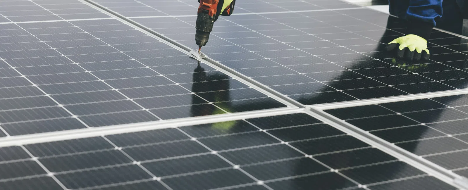 Technician installing solar panels using a power drill wearing gloves and blue workwear on a sunny day