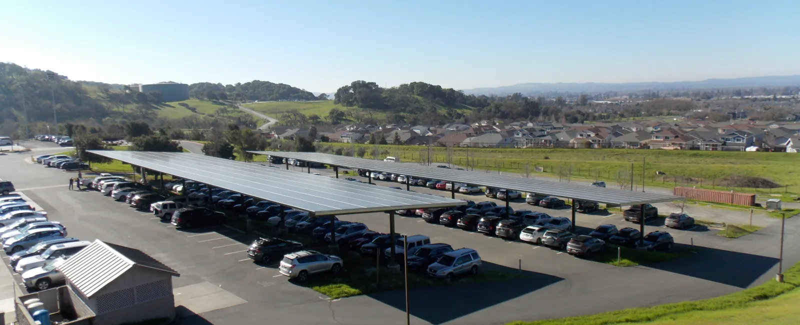Parking lot with solar panel canopies covering rows of parked cars under clear blue sky on a sunny day.