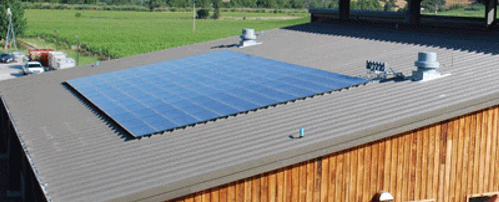 Aerial view of a modern building featuring solar panels on a metal roof in a green landscape.
