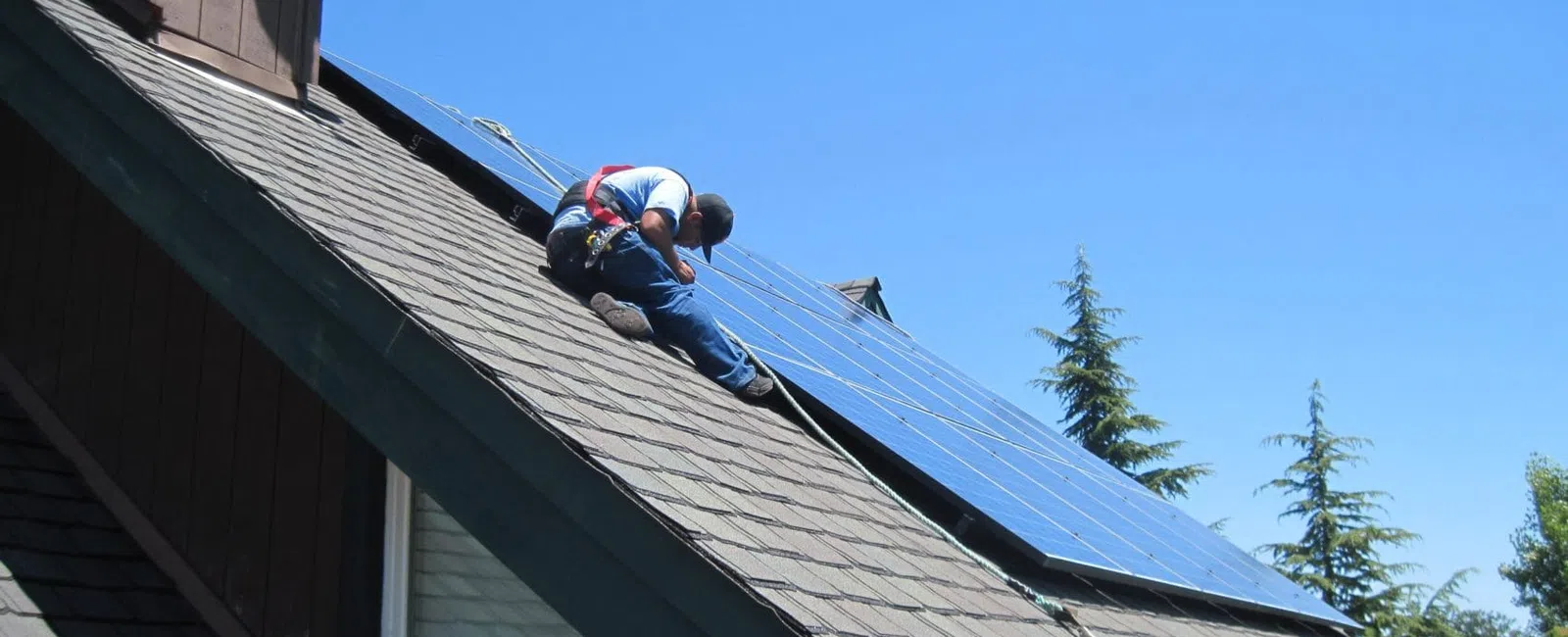 Worker installing solar panels on a sloped residential roof under a clear blue sky