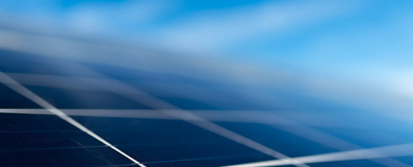 Close-up of dark blue solar panels with visible grid lines under a bright blue sky with wispy clouds