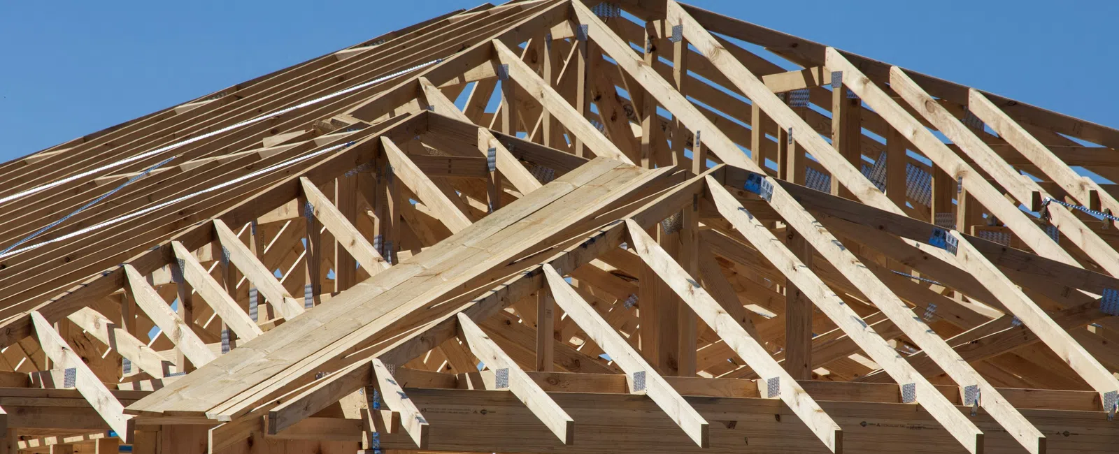 Wooden frame structure of a house under construction against a clear blue sky on a sunny day.