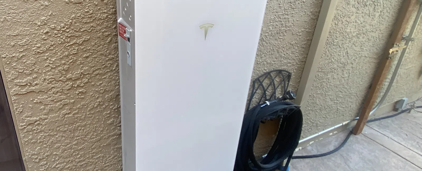 Tesla Powerwall mounted on a wall with wiring nearby in a modern home setting.