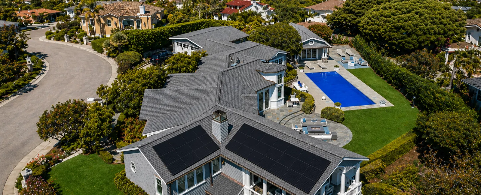 Aerial view of a large suburban house with solar panels on the roof and a backyard pool surrounded by greenery.