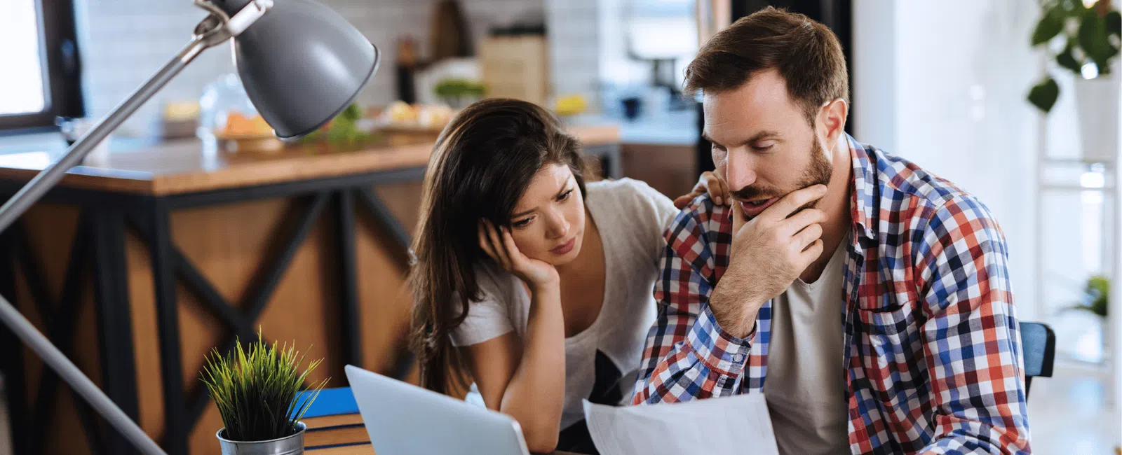 Couple reviewing bills and finances with laptop and documents at home, appearing concerned and focused