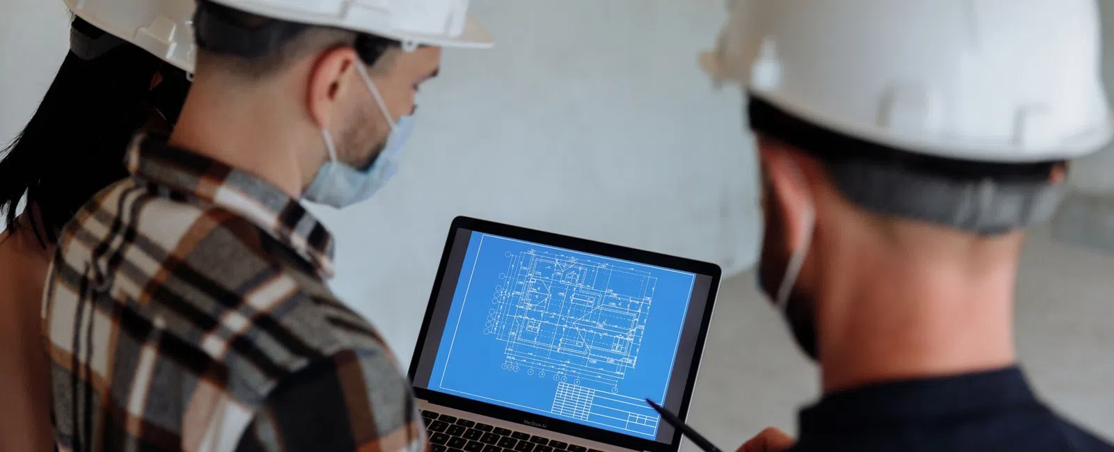 Construction professionals in hard hats reviewing building blueprints on a laptop at a work site.