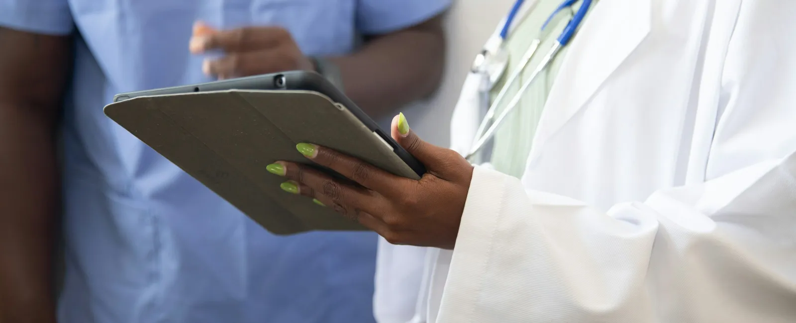 Close-up of a female doctor holding a tablet with a male nurse in scrubs in the background during consultation.