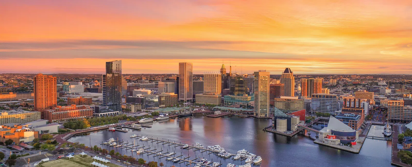 Baltimore Inner Harbor at sunset with city skyline, boats docked, and vibrant orange sky.