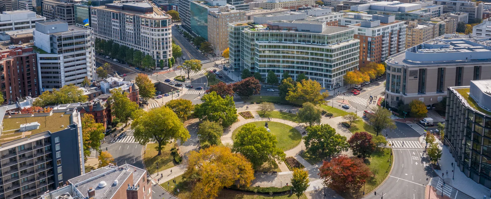 Aerial view of Washington DC featuring a circular park with trees surrounded by city buildings and the Washington Monument in the background.