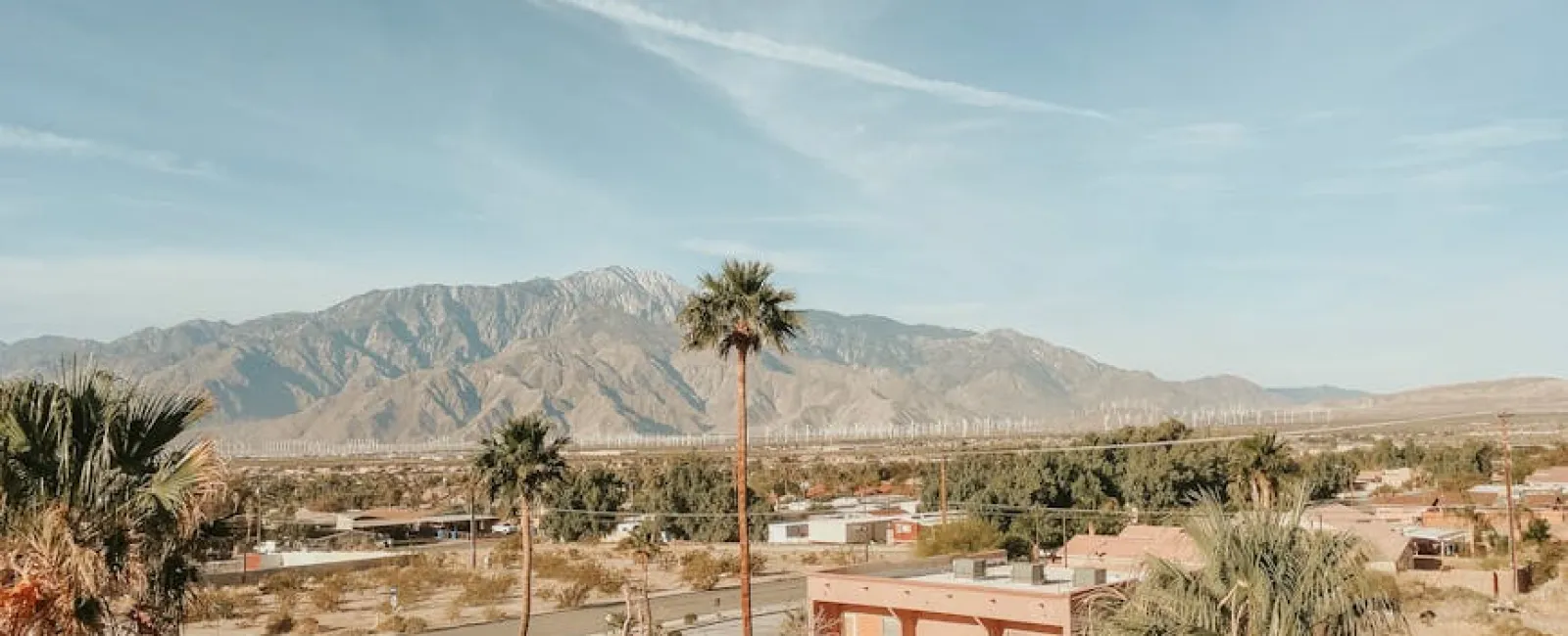 Desert townscape with palm trees, clear sky, and mountain range in the background under bright daylight.