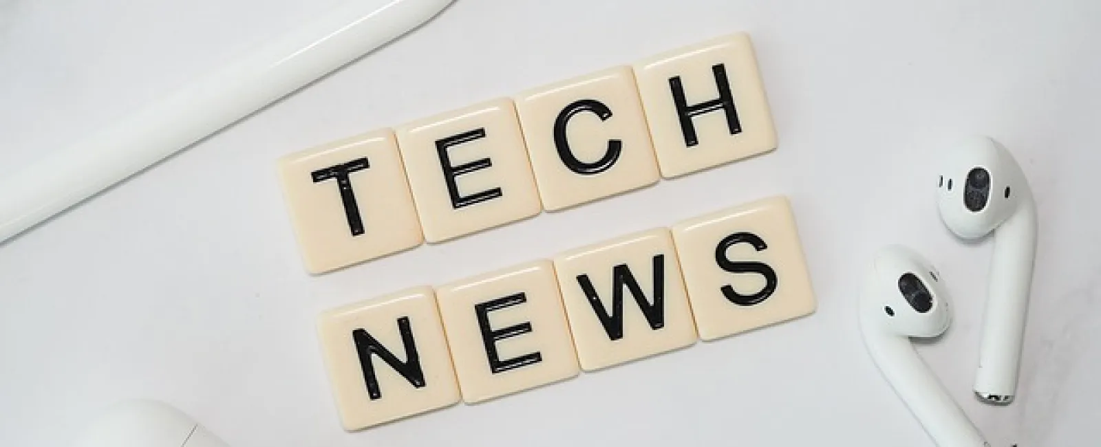 Tech news spelled with letter tiles next to white wireless earbuds, a pen, and charging case on a white surface.