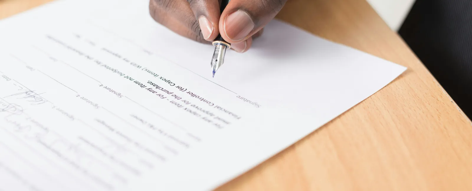 Close-up of a person signing a Managed IT provider contract with a silver pen on a wooden table