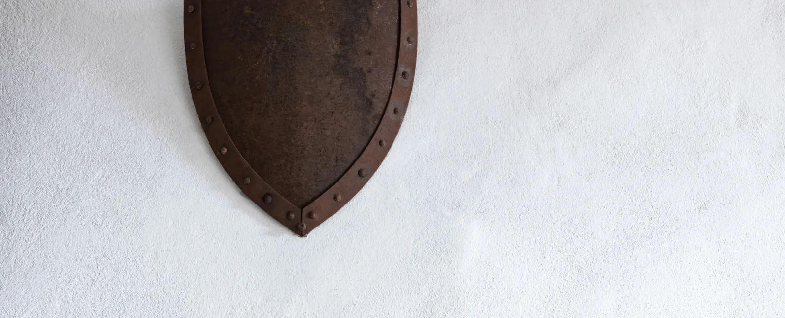 Rusty medieval metal shield with rivets mounted on a plain white textured wall referencing Guardian IT
