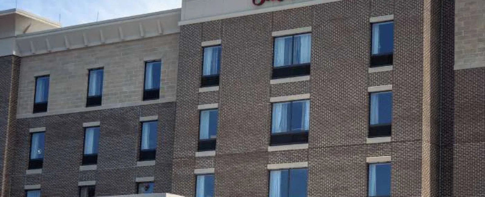 Exterior view of Hampton Inn & Suites hotel building with multiple windows and brick facade under clear sky