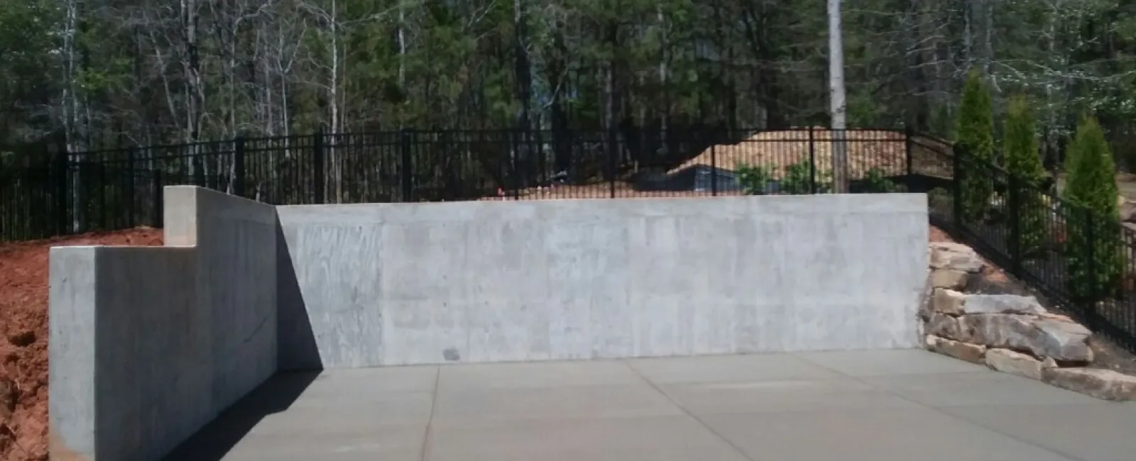 a concrete wall with a fence and trees in the background