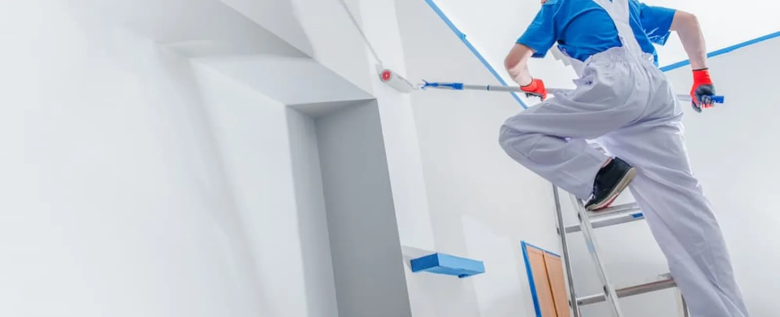 A professional painter in white overalls using a roller on a ladder, illustrating high-quality professional exterior painting for residential homes.