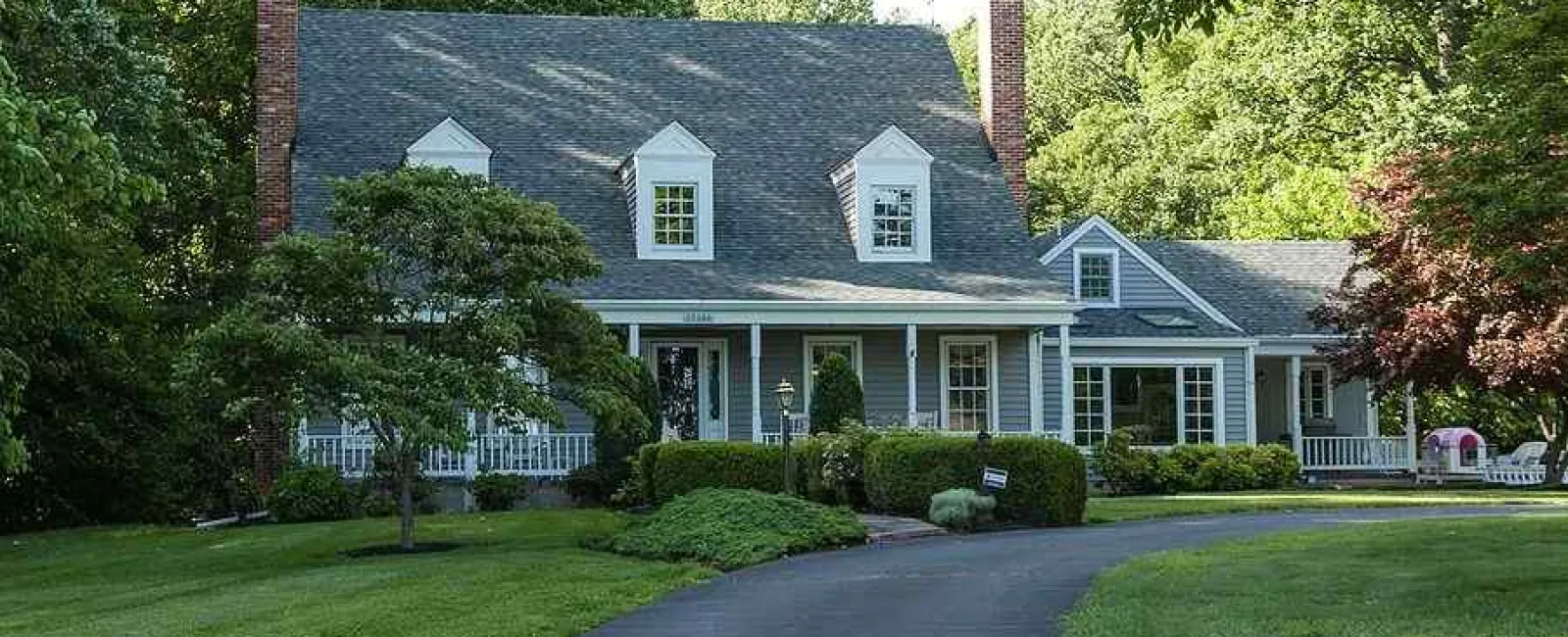 Large gray two-story house with white trim surrounded by trees and a curved driveway leading to the entrance