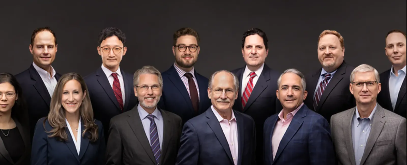 Group portrait of twelve diverse business professionals in formal attire against a dark background