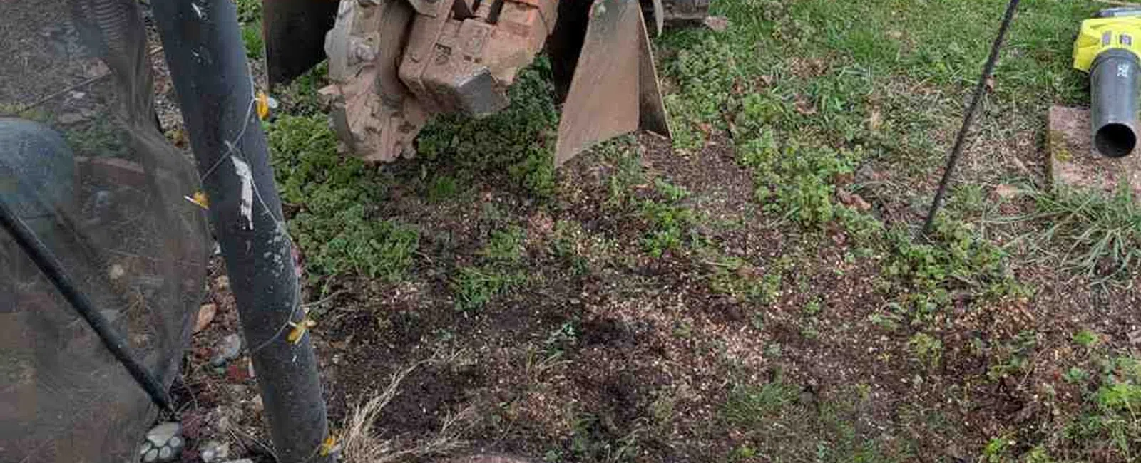 Orange stump grinder in a backyard clearing a tree stump near a patio and green grass area.