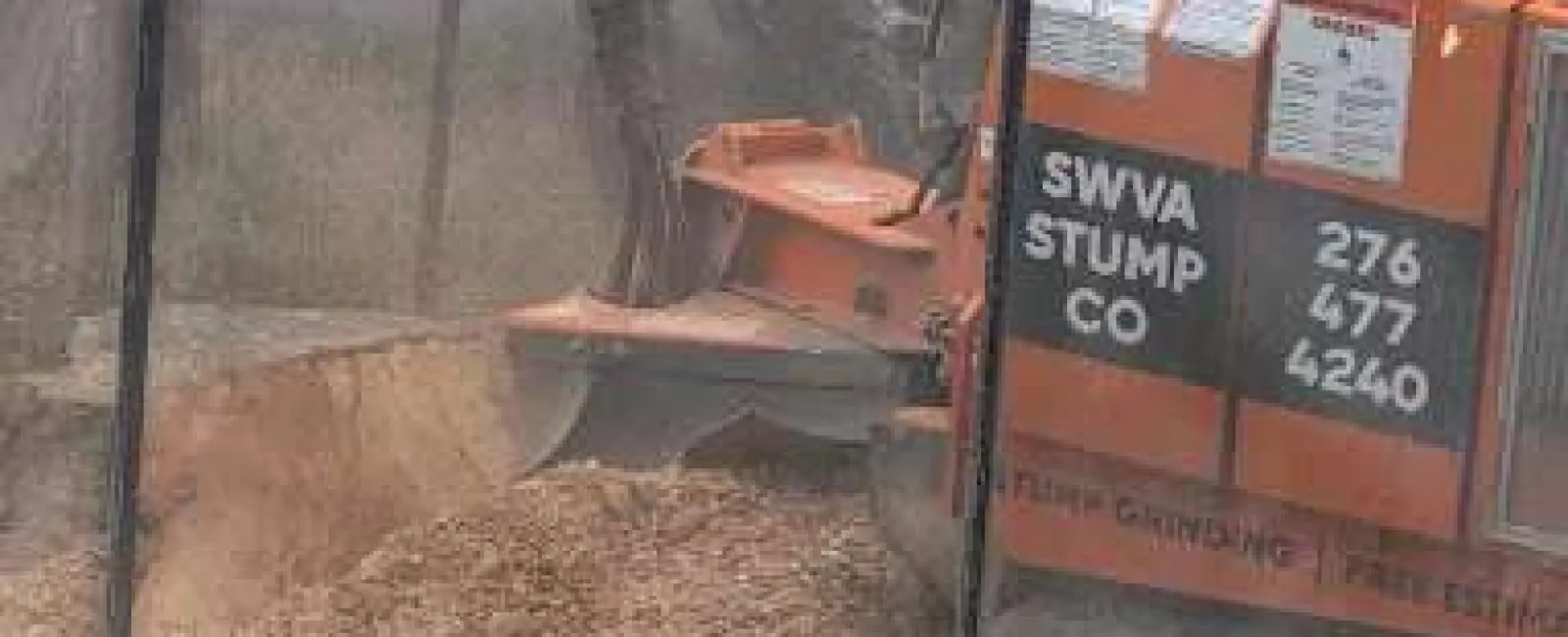 Orange stump grinding machine removing tree stump outdoors with protective mesh screen and operator nearby