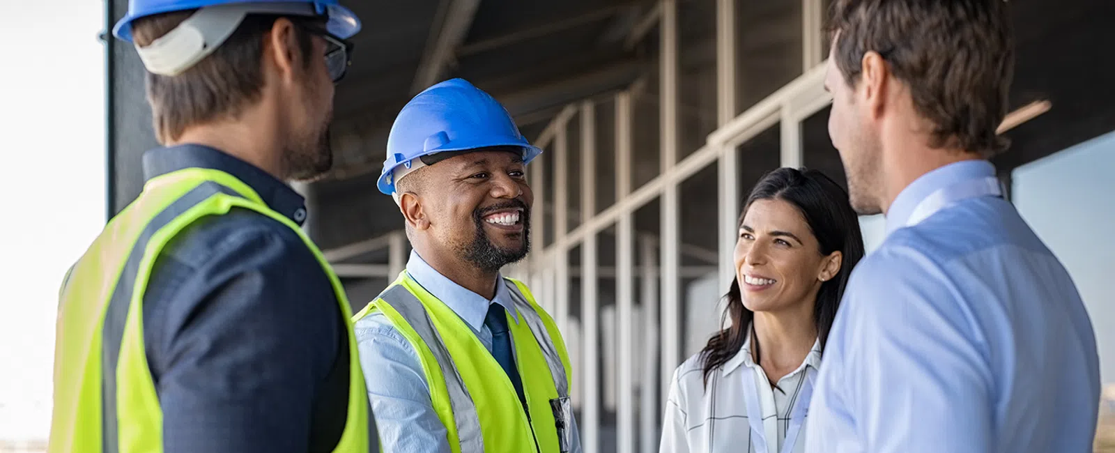 Construction professionals wearing safety gear shaking hands and smiling during a site meeting on a building balcony