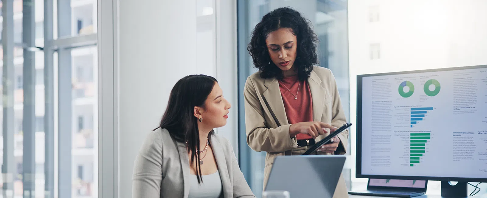 Two women examine data on a tablet.