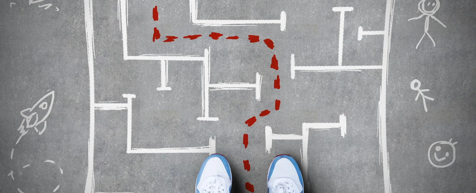 Person wearing sneakers stands before a chalk-drawn maze with a red path leading to the exit on concrete.
