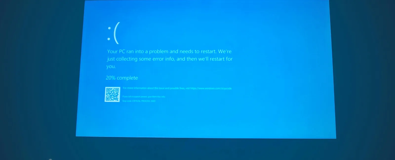 Blue screen error on a computer showing a sad face emoticon and system restart message at 20% progress.